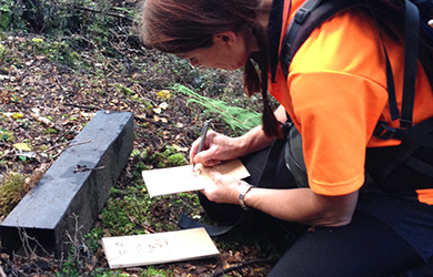 A volunteer in a bright orange shirt writes notes while crouched next to a tracking tunnel - a rectangular wooden box.