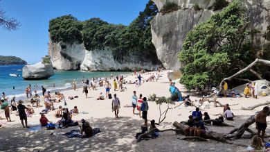 A busy, small beach butted up against cliffs.