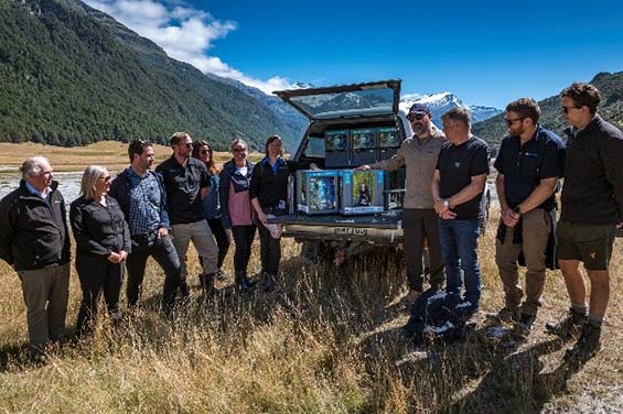 A group of people stand around a ute with an open boot.