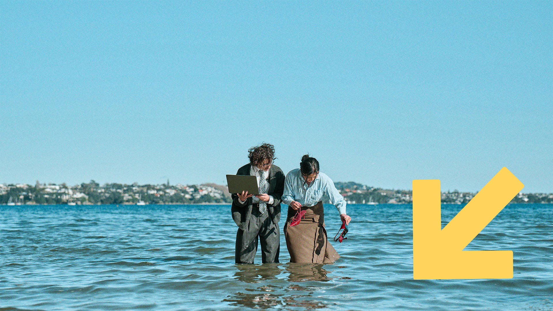 Two people in business attire  stand knee-deep in the sea.