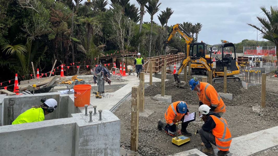 A busy construction site with five people scattered across various work areas in hi-vis jackets.