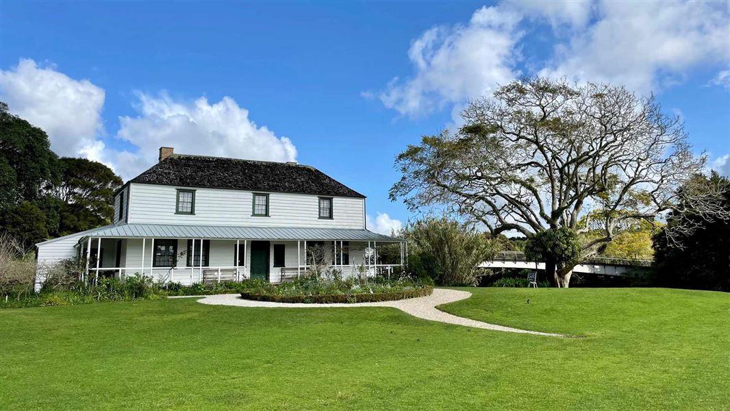 White, weather board, historic home in landscaped garden. 