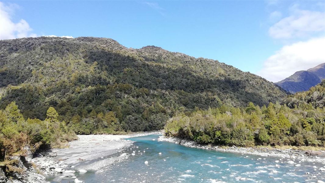 A river curves before a forested steep hill.