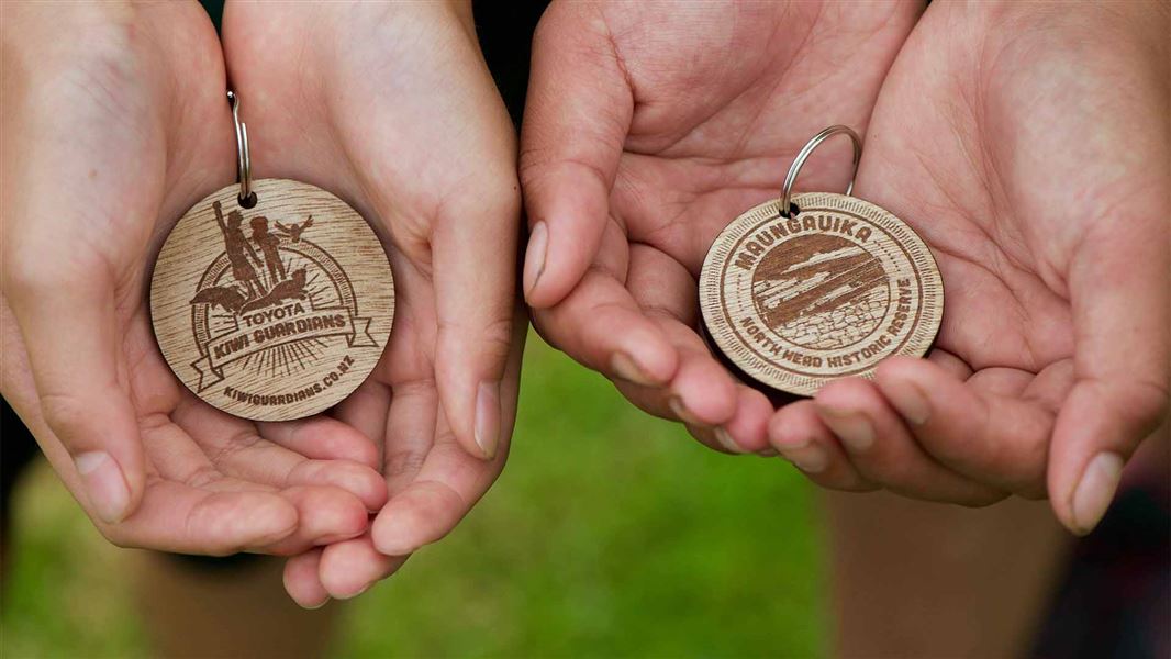 Two kiwi guardian medals held in two peoples hands.