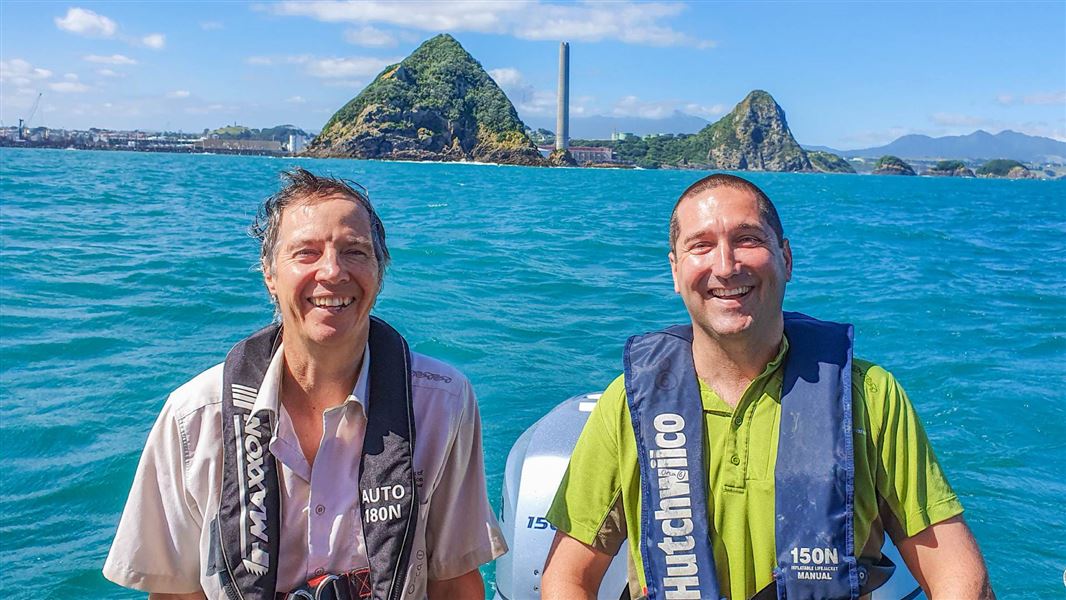 Two men standing on a boat together on a sunny day.