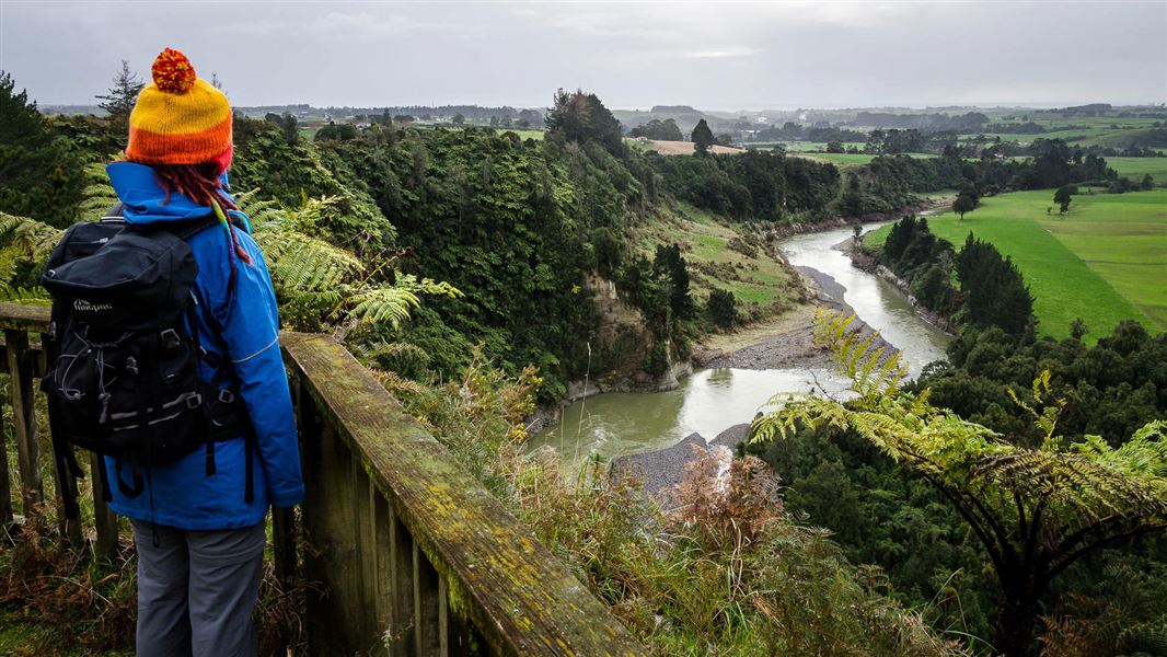 Person standing by railing looking over river.