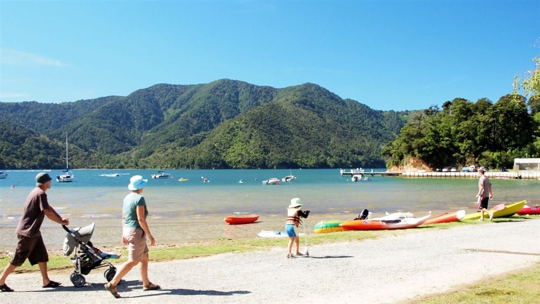 A family waking by a lake while kayaks line the water's edge. 