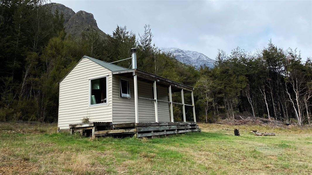 Small wooden building on grass near trees.