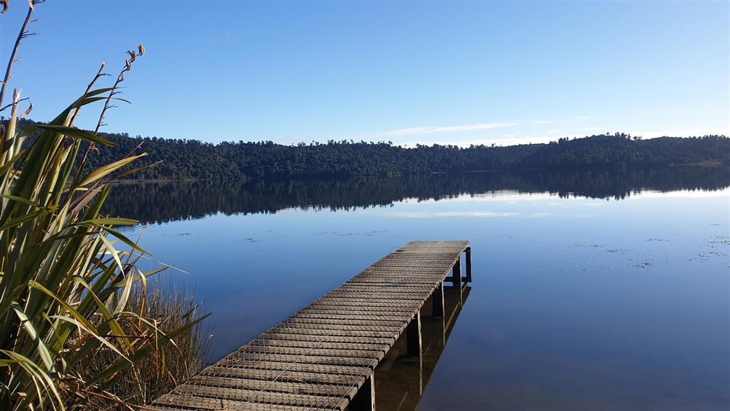 Jetty on a blue lake wiht bush surrounding the lake. 