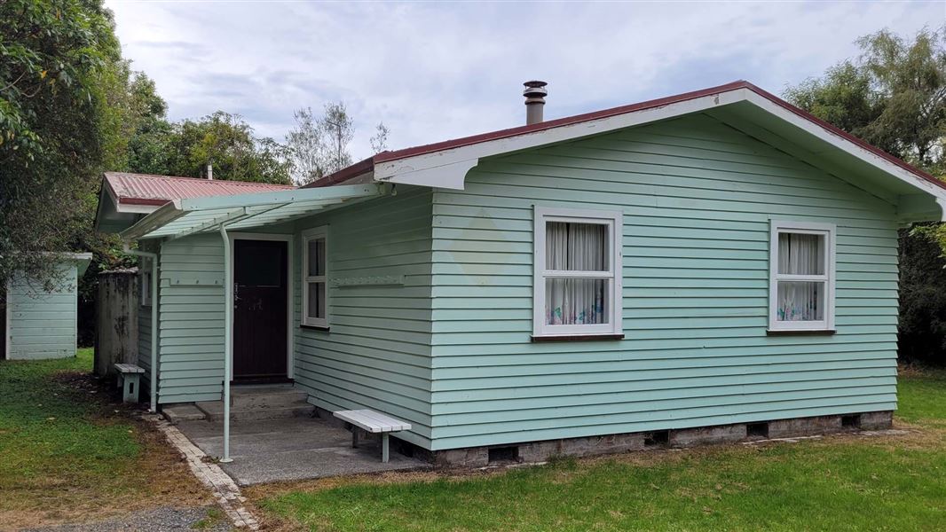 Green weatherboard lodge with small verandah. 