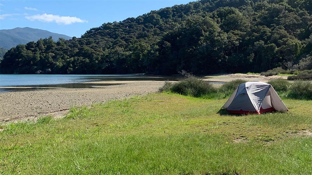 Tent on grassy flat by hill.