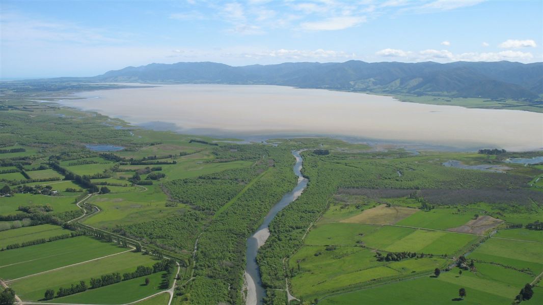 An aerial view of a river running across lush green lands to the sea.