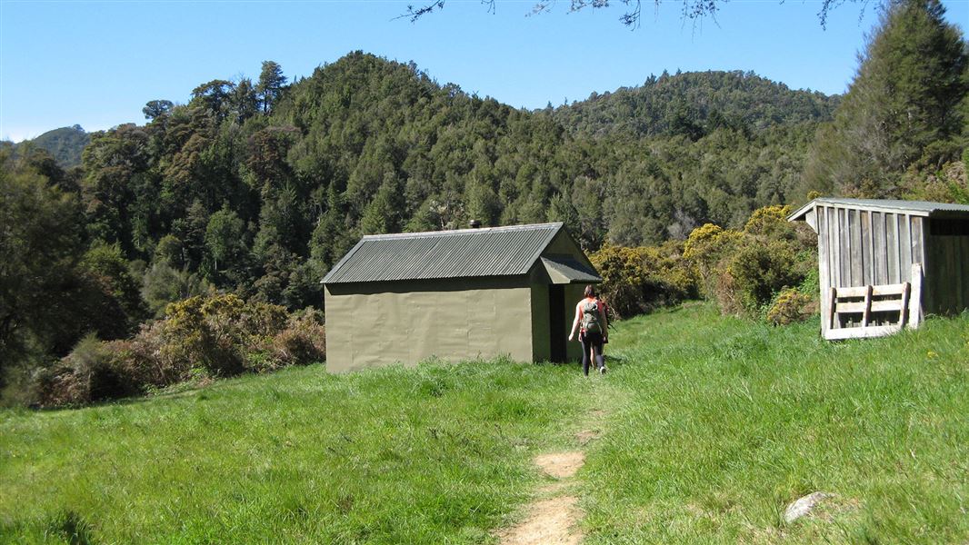 Small building on grass by trees.