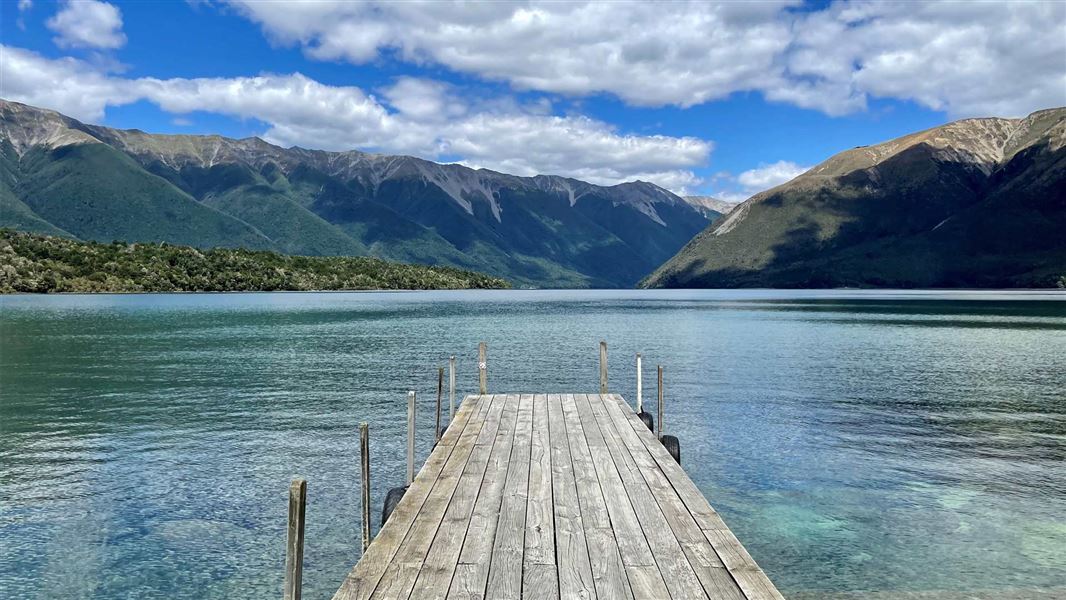 Jetty leading out to large lake with mountain range in the background.