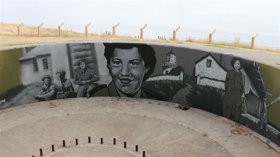 A circulate concrete enclosure with a large mural depicting female soldiers and young men around the emplacement.