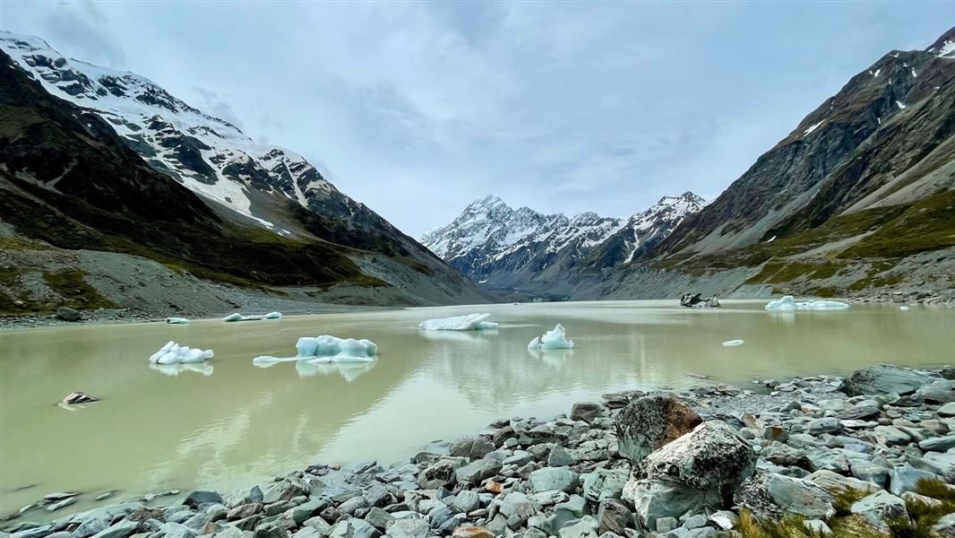 Glacial lake with ice bergs and snow capped mountains behind.