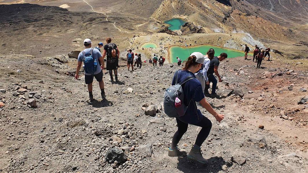 People descending a steep slope on scree towards Emerald Lakes. 