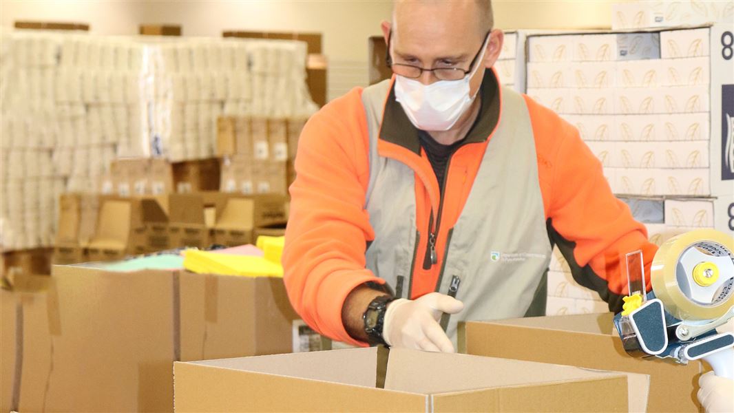 A man wearing a face mask packing a box of hygiene supplies.