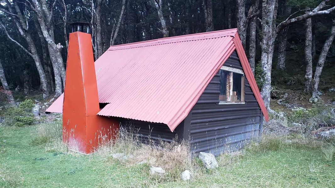 A small red hut made from roofing tin surrounded by forest.