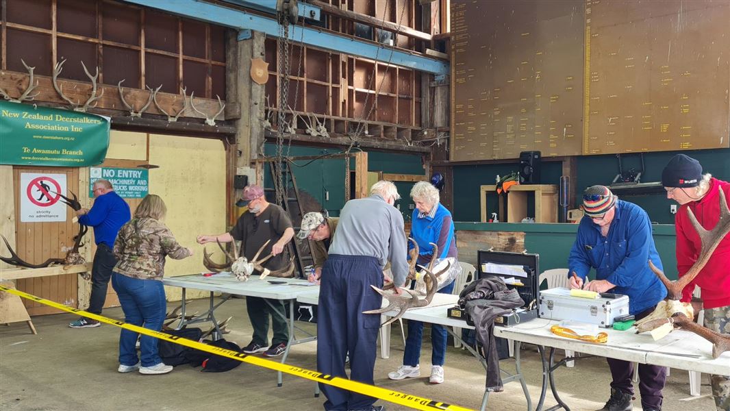 A long table with several people standing nearby holding antlers or taking notes.