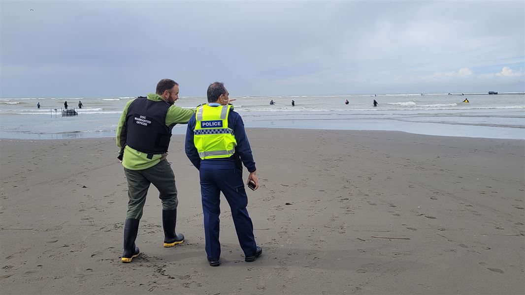 Main on beach standing next to police officer gestures out to sea.