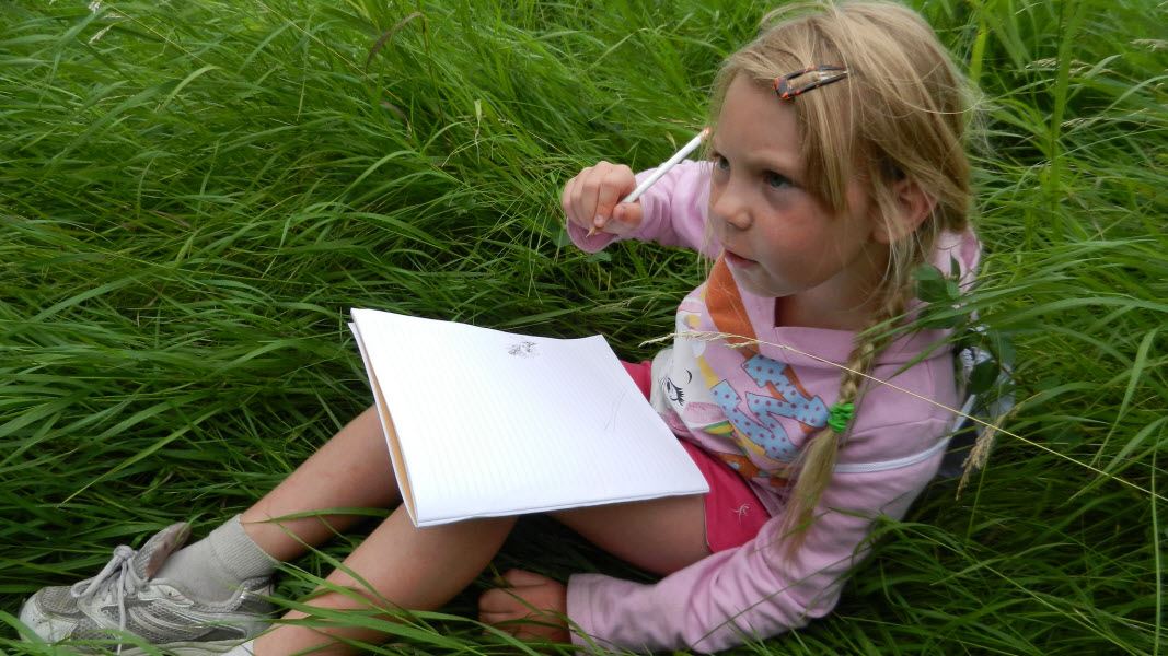 Child in grass writing in a journal. 