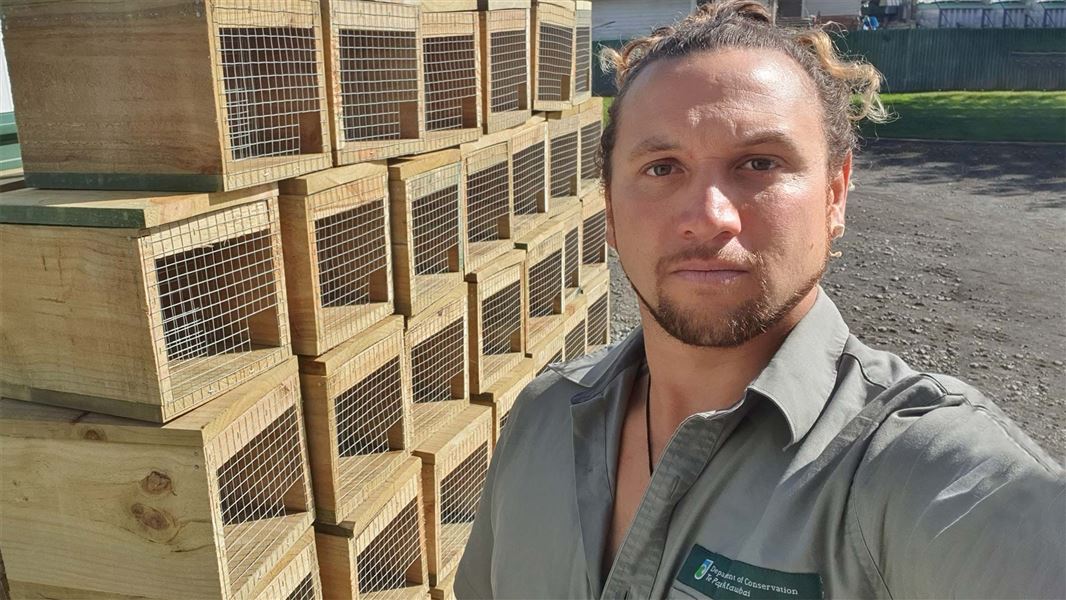 A man close standing close to camera, with a tall pile of traps set behind him.