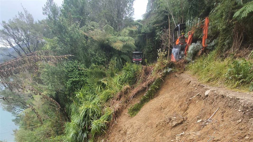 A man operates a digger on a steep bank to clear a slip.