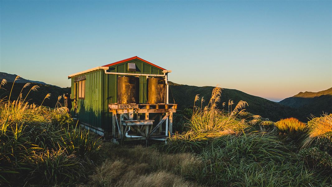 Small wooden building by hills and grasses.