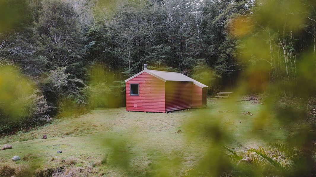 Small red building in grassy area with trees nearby.