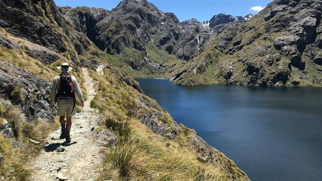 Tramper walks along side Lake Harris on the Routeburn Track.