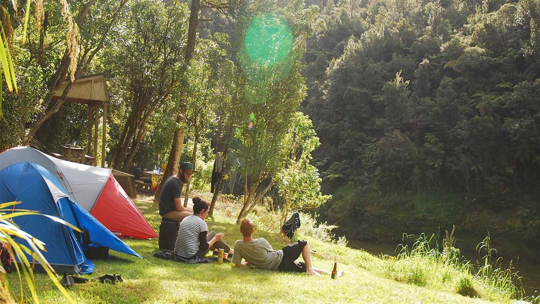 Campers relax in the sun on the grass in front of their tents, next to the Whanganui River. 