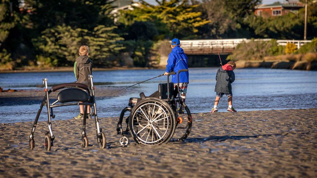 Children fishing with wheelchair on beach. 