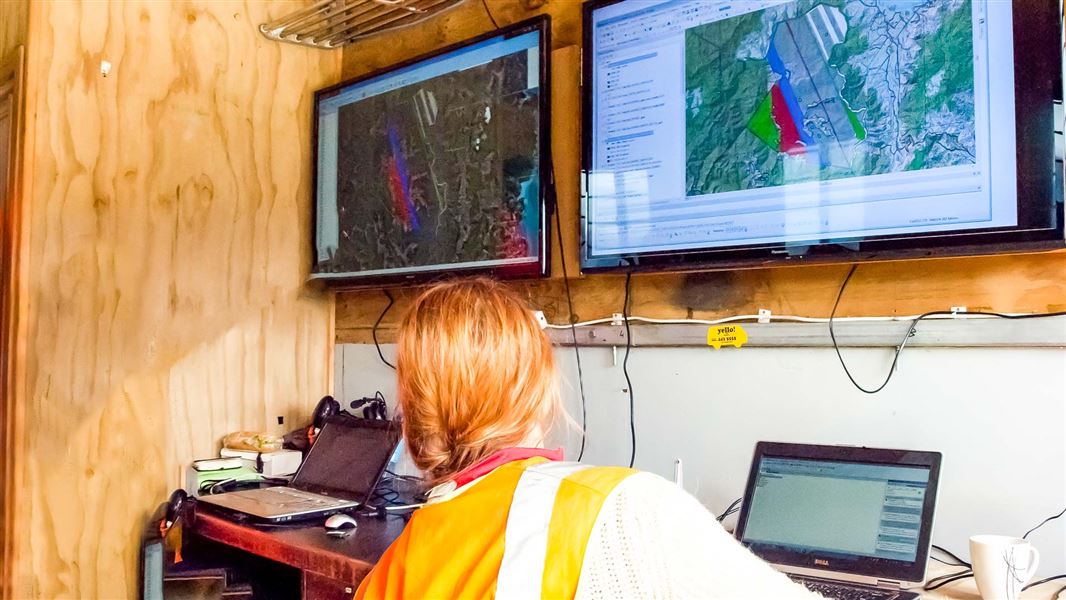 A woman looking across four screens of maps and flightpath data.