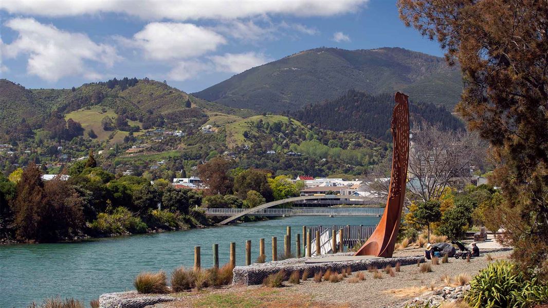 An end of a waka juts out of a the ground next to a river.