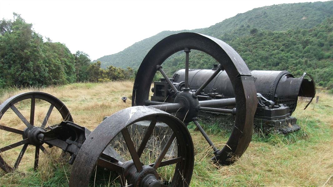 An old metal sawmill with three large wheels and a machinery part sitting in a paddock. 