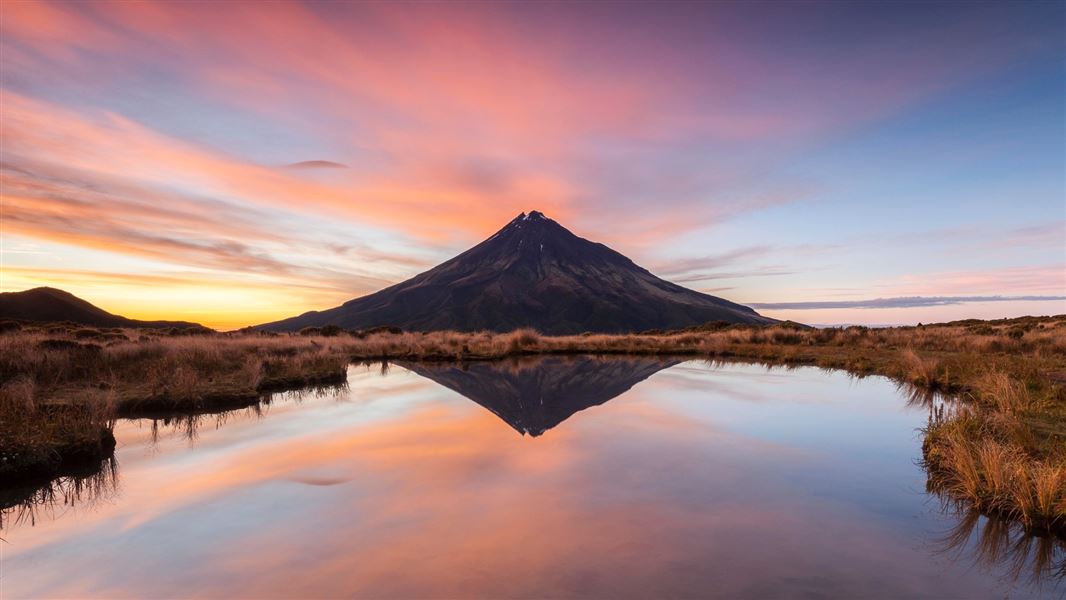 A picture from across the lake in front of Mount Taranaki, framed by a purple sky at dusk.