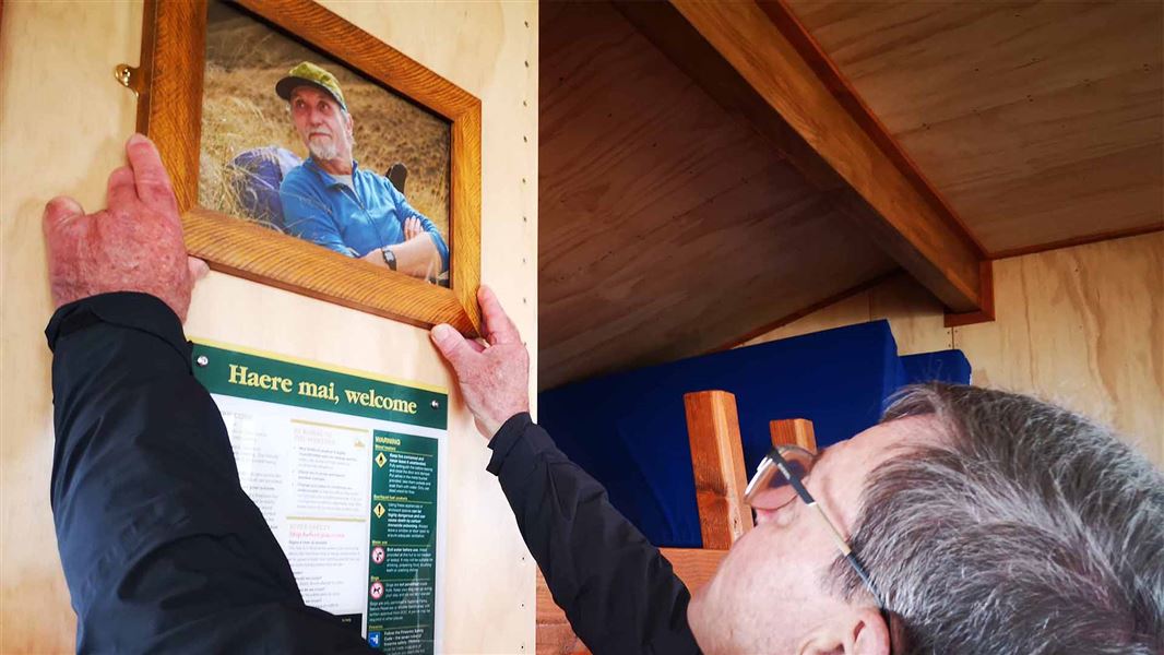 A person installing a photo of someone onto the wall of a hut.