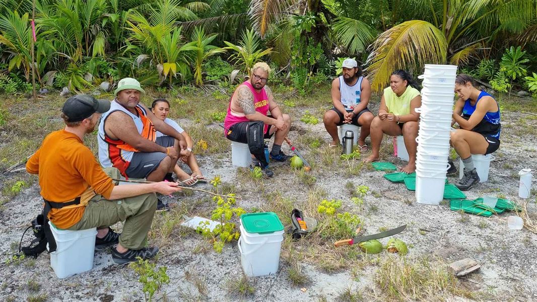 Group of people sitting in a semi circle on the beach talking. 