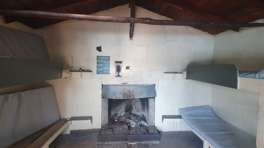 View of the inside of a hut with bunk beds on each side and a fire place in the middle.