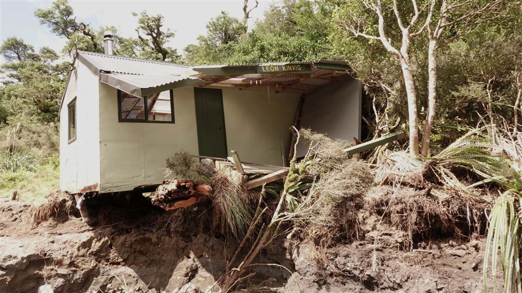 A damaged white hut is perched precariously on the edge of an eroded bank.