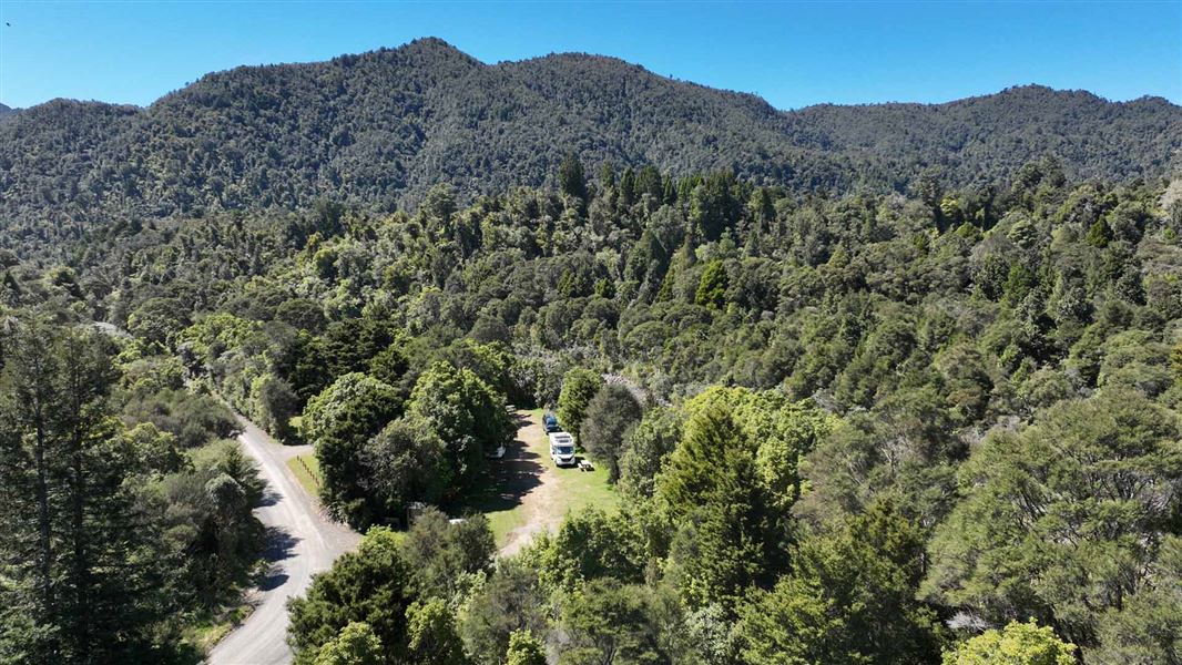 Aerial image of campsite surrounded by forest and a few campervans parked under the trees. 
