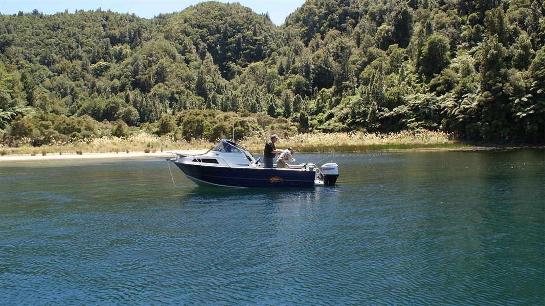 A small boat with a person fishing out the back of it on a small lake.