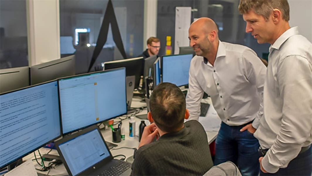 One man on a computer with two colleagues looking over his shoulder