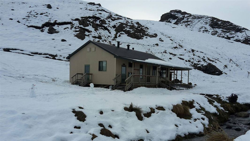 Hut in rocky area surrounded by snow.