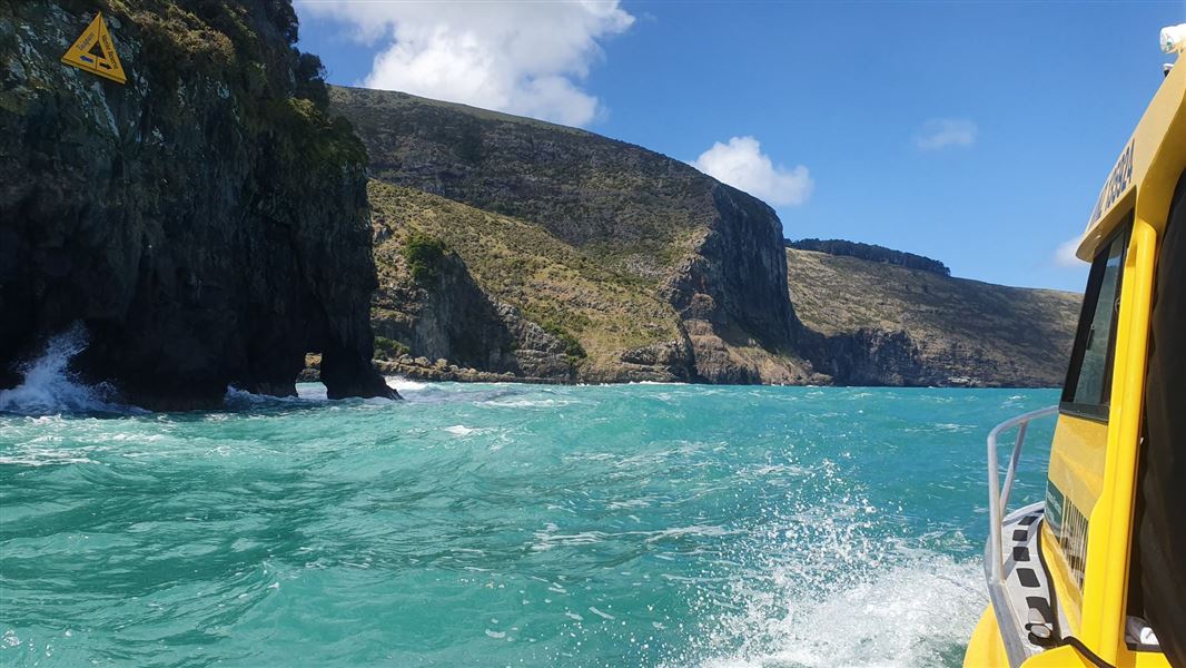 A boat passing high cliffs on clear blue waters.