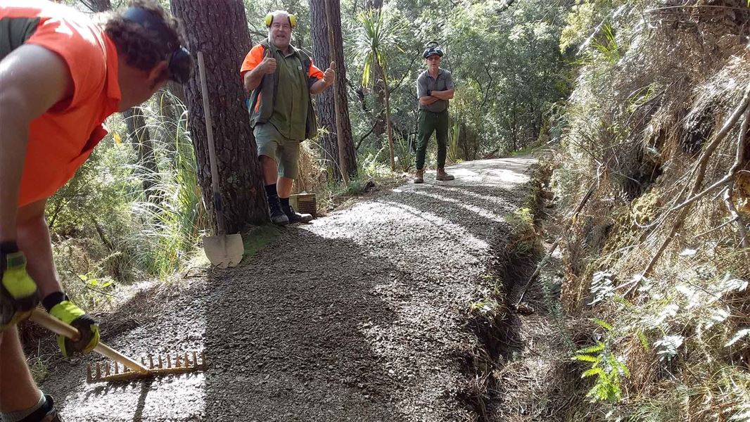 Three people help to spread gravel on the track.