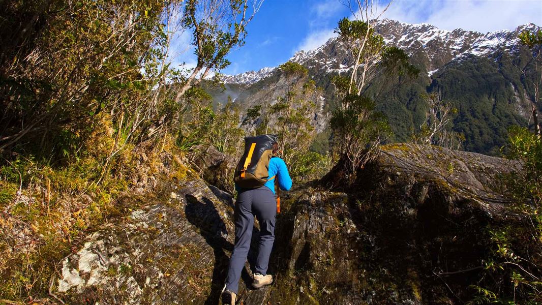 Hiker walking up steep slope with mountain range behind.