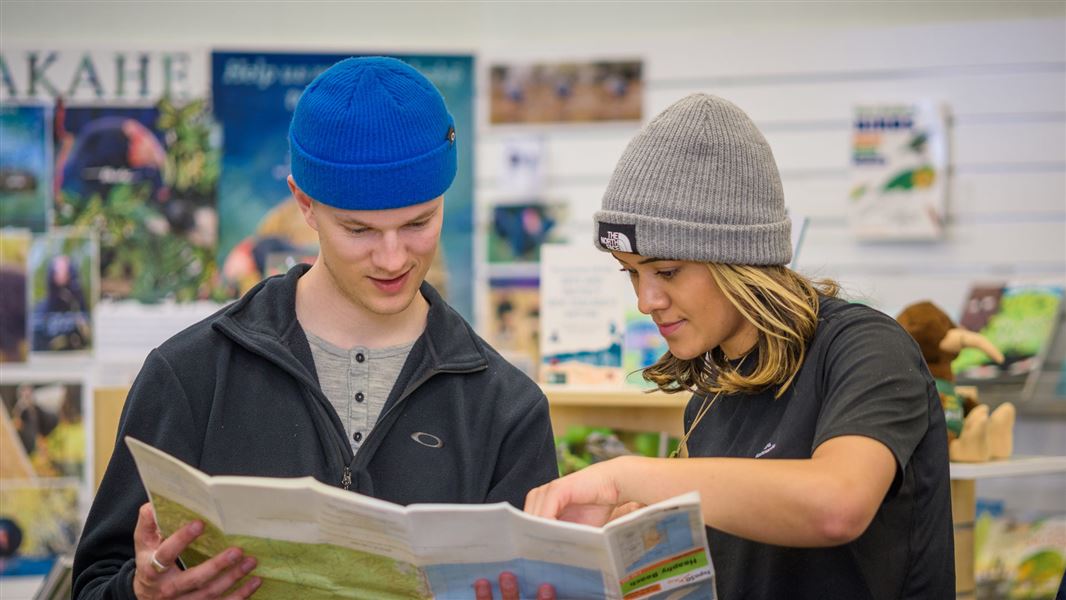 Two people reading a map in a DOC visitor centre. 