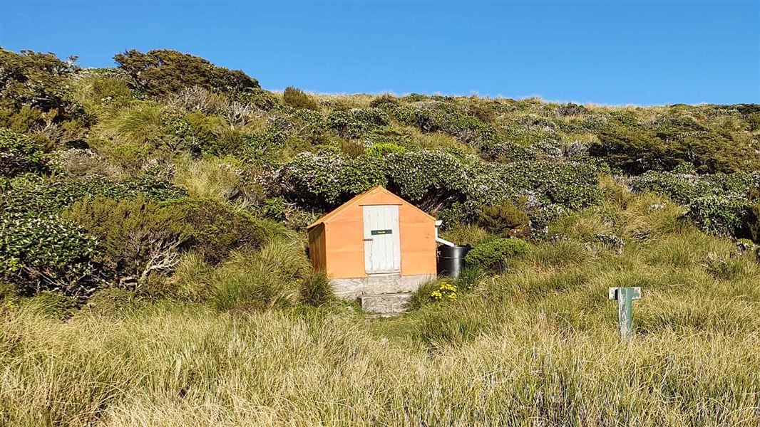 A small orange hut with a white door sits nestled in a grassy hillside. 